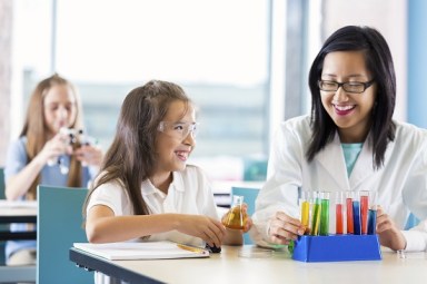 Asian teacher helping elementary school girl with chemistry project