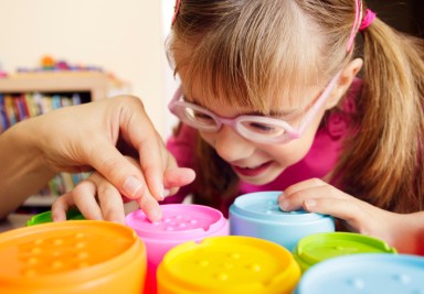 Smiling child with disability touching textured cups with her teacher