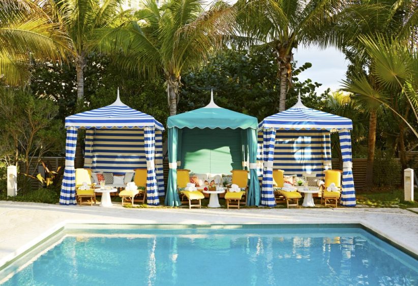 three cabanas with striped awnings and beach chairs, set up next to pool at fancy resort