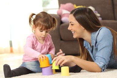 babysitter and child playing with colorful toys on the floor