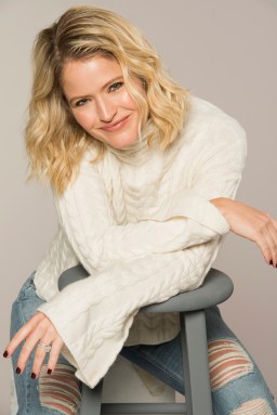 sara haines in white sweater and jeans leaning on stool