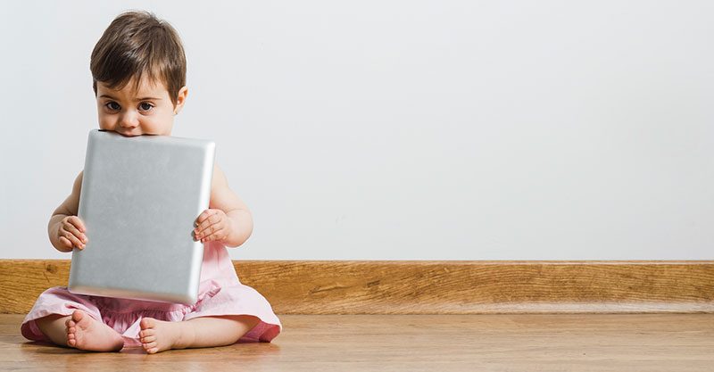 toddler holding ipad sitting on wood floor