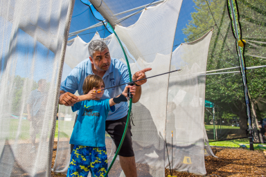 young boy getting bow and arrow instruction at camp from an adult counselor