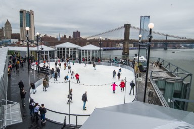 skaters on a rooftop ice rink with the brooklyn bridge in the background