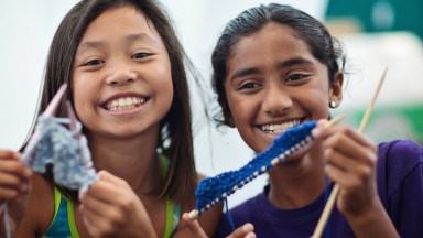 two young girls at summer camp doing a knitting activity