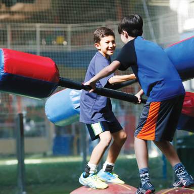 two boys balance standing on red balls while they joust with inflatable boppers