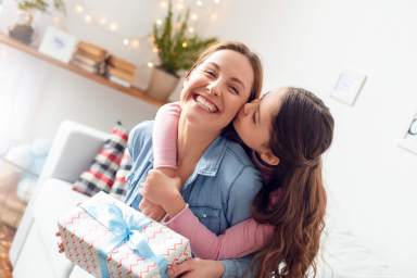 Mother and daughter at home mother’s day sitting daughter hugging mom kissing cheek joyful