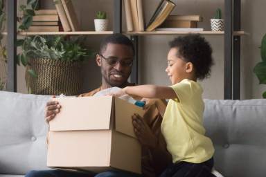 Happy african father and little son opening parcel at home