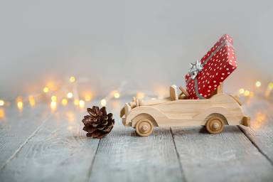 wooden car with gift on a wooden gray background and lights from the garland. Christmas concept