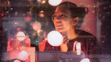 Young beautiful Asian woman feel good with the New Year celebrations with gift box in home decorate with christmas tree.Concept of happy holidays.Glass window reflection and snow effect.