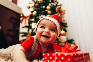 Baby playing with gift box on the living room floor over christmas tree lights on background