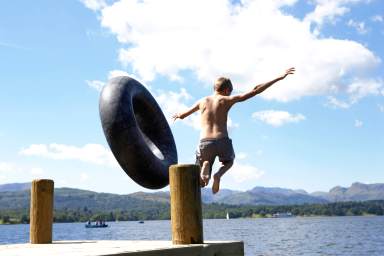 Boy (11-13) leaping from lake jetty with rubber ring, rear view