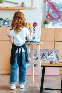 back view of redhead kid painting on canvas