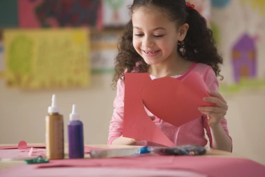 Hispanic girl cutting out Valentine’s heart in classroom