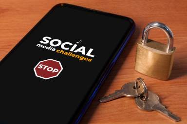 Smartphone showing the message “stop social media challenges” a wooden table with a lock and keys.