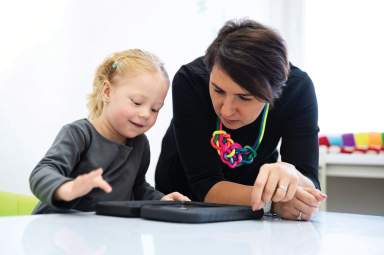 Toddler girl in child occupational therapy session doing playful exercises on a digital tablet with her therapist.