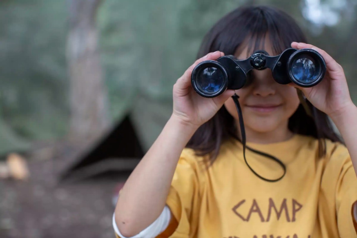 Portrait cute girl bird watching at summer camp with binoculars