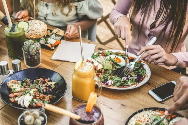 Hands view of young people eating brunch and drinking smoothies bowl with ecological straws in plastic free restaurant – Healthy lifestyle, food trends concept – Focus on top fork dish