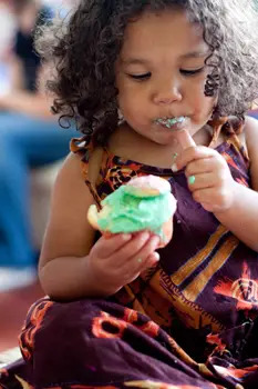 little girl eating a cupcake; young girl covered in frosting, eating cake