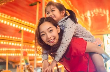 happy asia mother and daughter have fun in amusement carnival park with farris wheel and carousel background